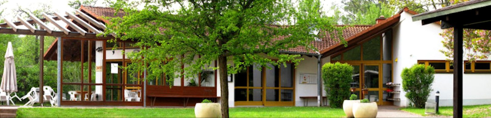 Das Clubhaus der Kelkheimer Tennisfreunde 77 mit Terrasse, davor Rasen und Bäume